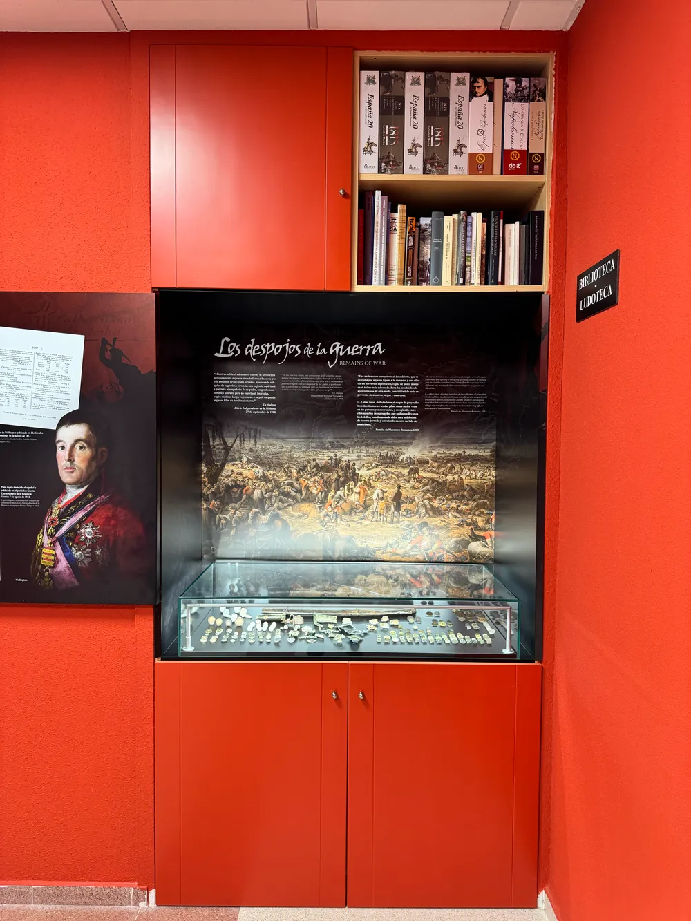 Panel con una pintura de la batalla y el retrato del duque de Wellington, junto a una vitrina con objetos de época y una pequeña biblioteca.