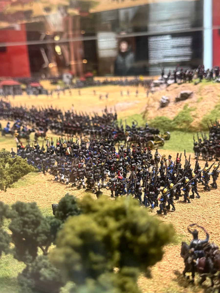 Detalle de la maqueta: columnas de soldados en miniatura avanzando entre árboles por el campo de batalla.